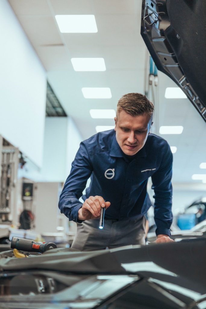 Mann på bilverksted lyser ned i motorrommet på en bil