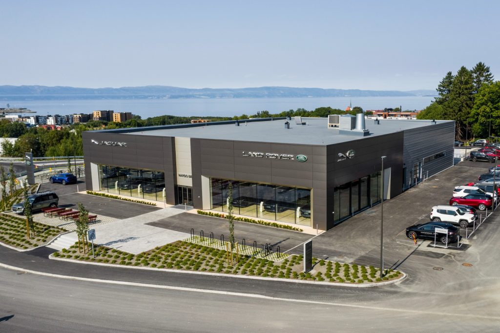 Firekantet, grå bygning med biler parkert utenfor