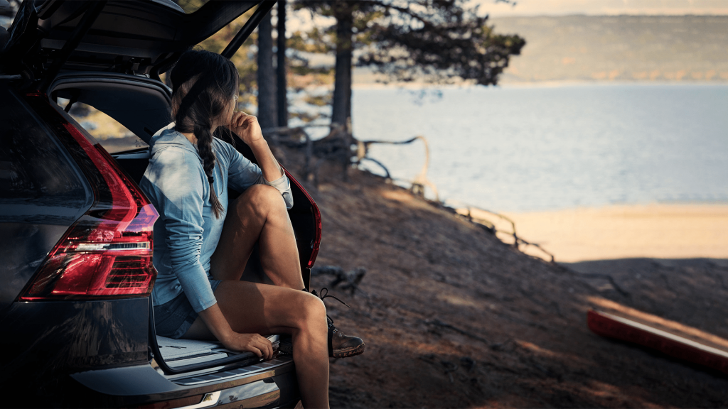 Kvine sitter i bagasjerommet til en bil som er parkert ved et vann