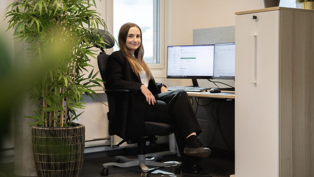 Kvinne sitter på et kontor foran to skjermer