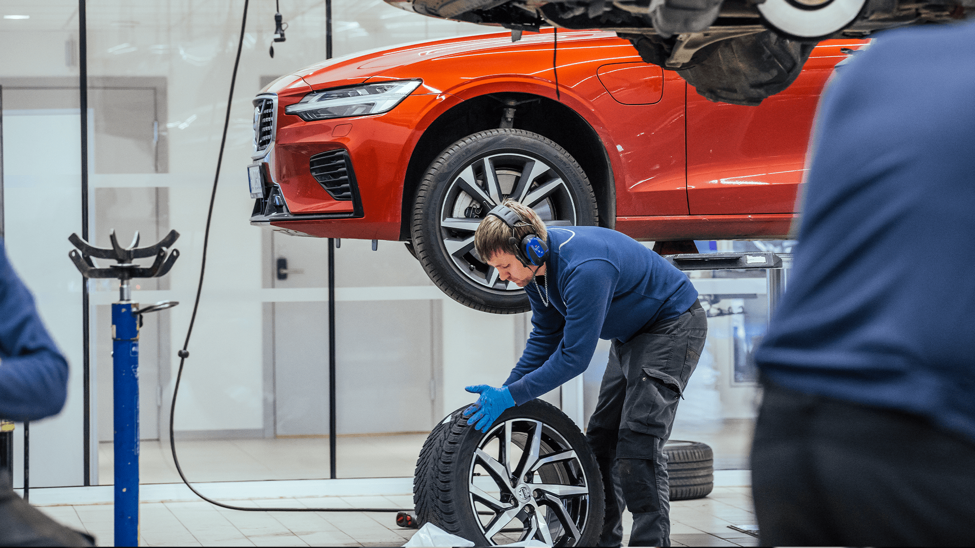 Mann skifter dekk på en hevet rød bil på verksted