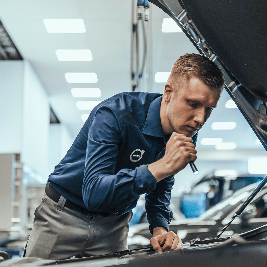 Mann lyser ned i motor på en bil på bilverksted