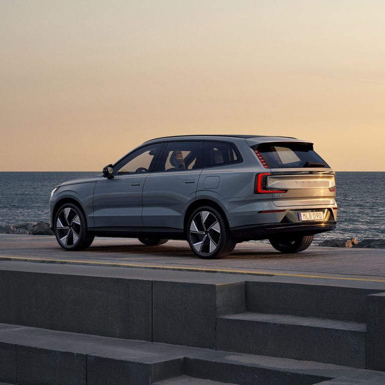 Sølvfarget EX90 stående på et platå foran sjø