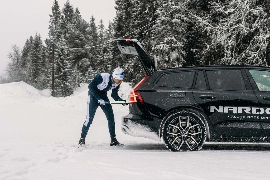 Mann legger et par skistaver inn i svart Volvo