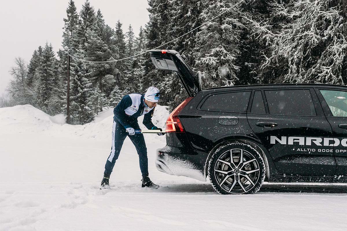 Mann legger et par skistaver inn i svart Volvo