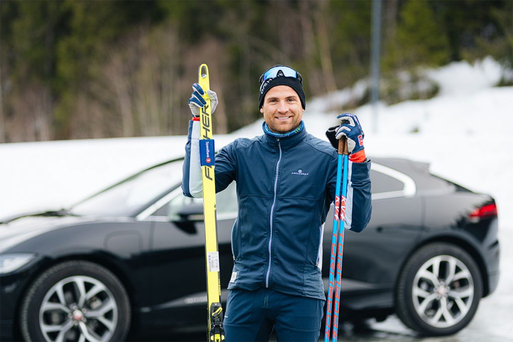 Niklas Dyrhaug holder et par langrennski og staver foran en sort bil