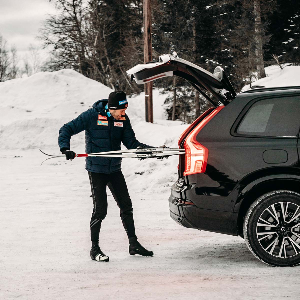Emil Iversen legger et par langrennski inn i bagasjerommet til en svart Volvo