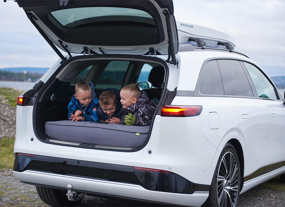 Tre barn ligger i bagasjerommet til en hvit Xpeng G9