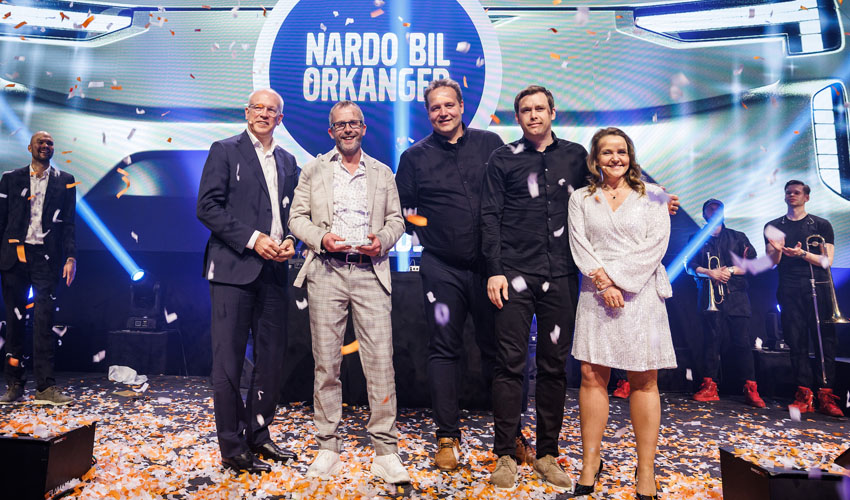 Fem personer på en scene under en prisutdeling med lys bak